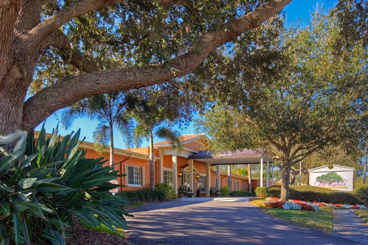 Front entrance of Wrights Healthcare & Rehabilitation Center with a covered driveway, landscaped flowerbeds, and large trees.