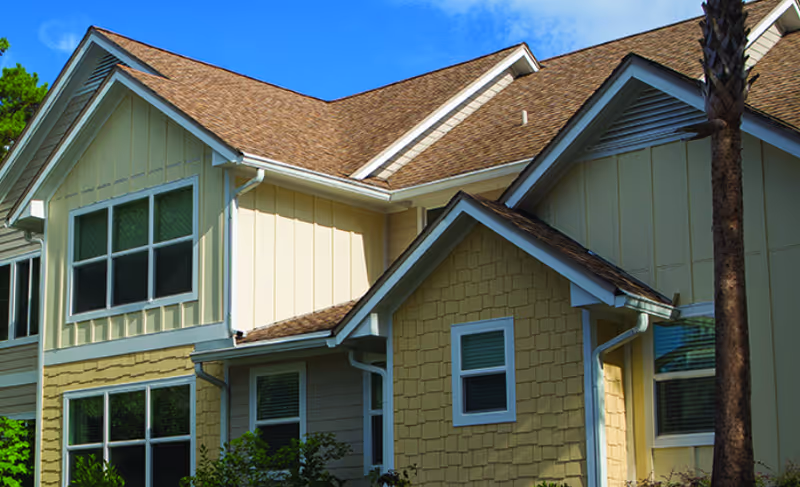 Exterior front of a yellow multi-story residential building with pitched roofs and windows under a blue sky.