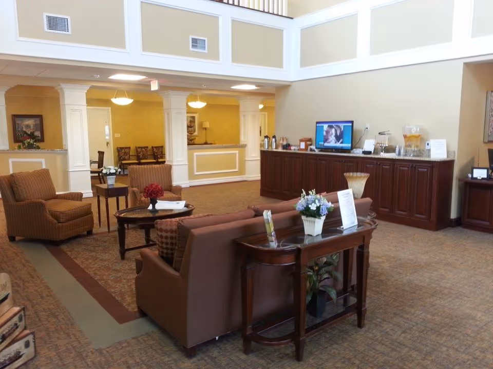 Spacious assisted living lobby with sofas, armchairs, a coffee table, and a long refreshment counter under a high ceiling.