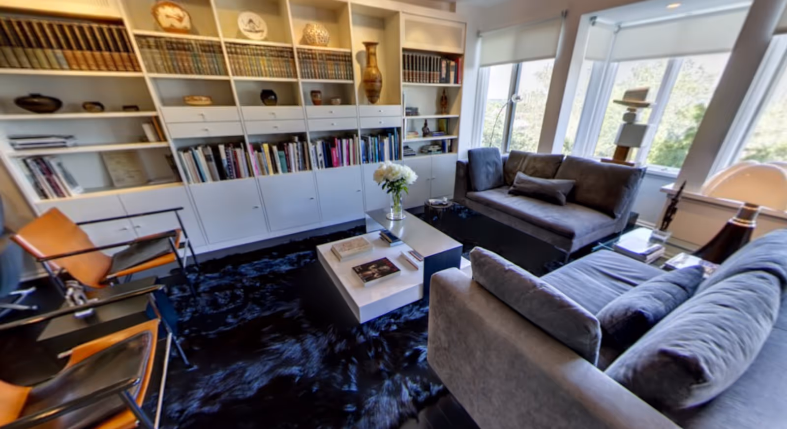 Bright living room with two gray sofas, a central coffee table, built-in bookshelves and large windows.