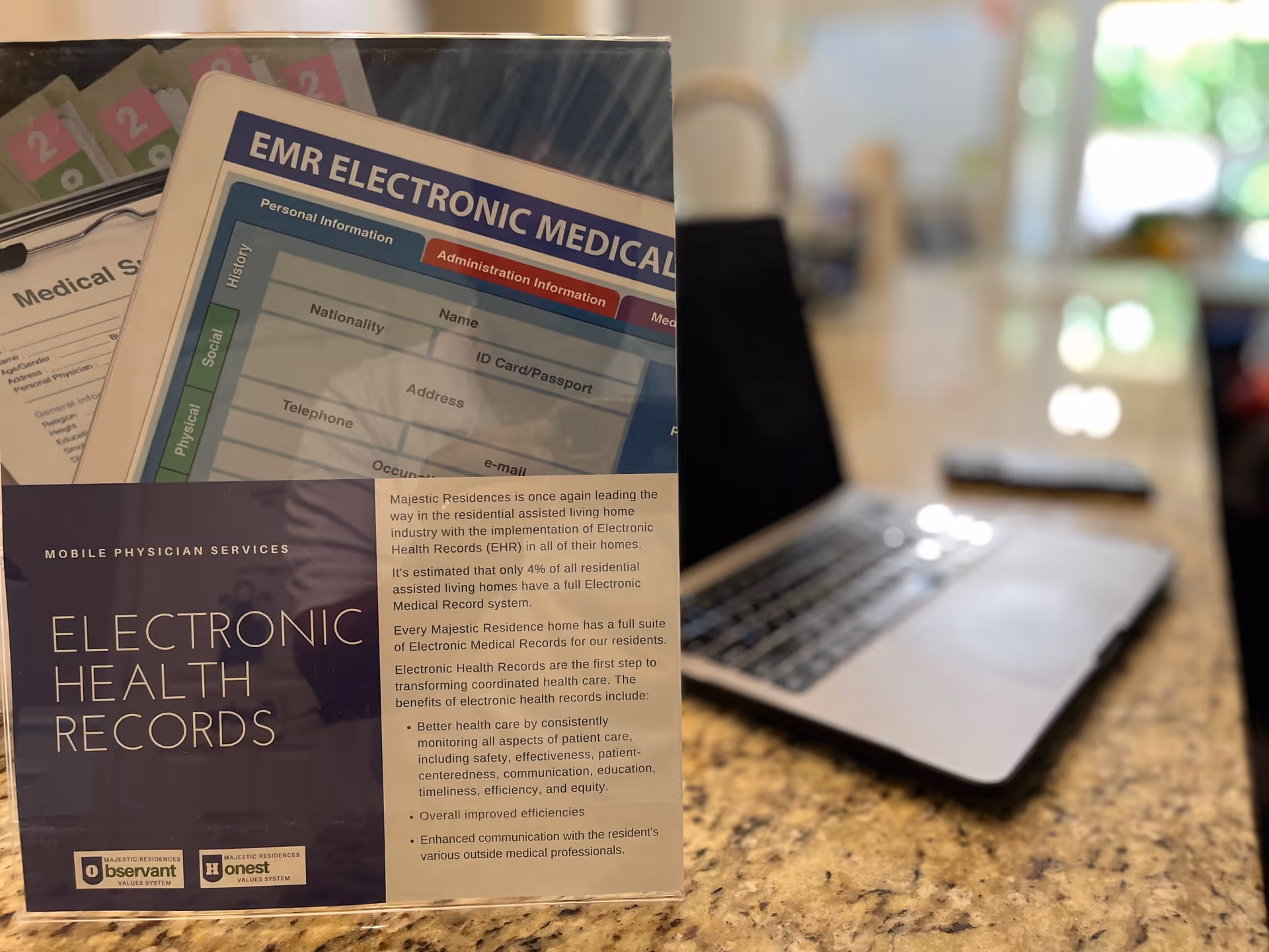 A tabletop brochure about Electronic Health Records sits on a granite counter in front of a blurred open laptop.