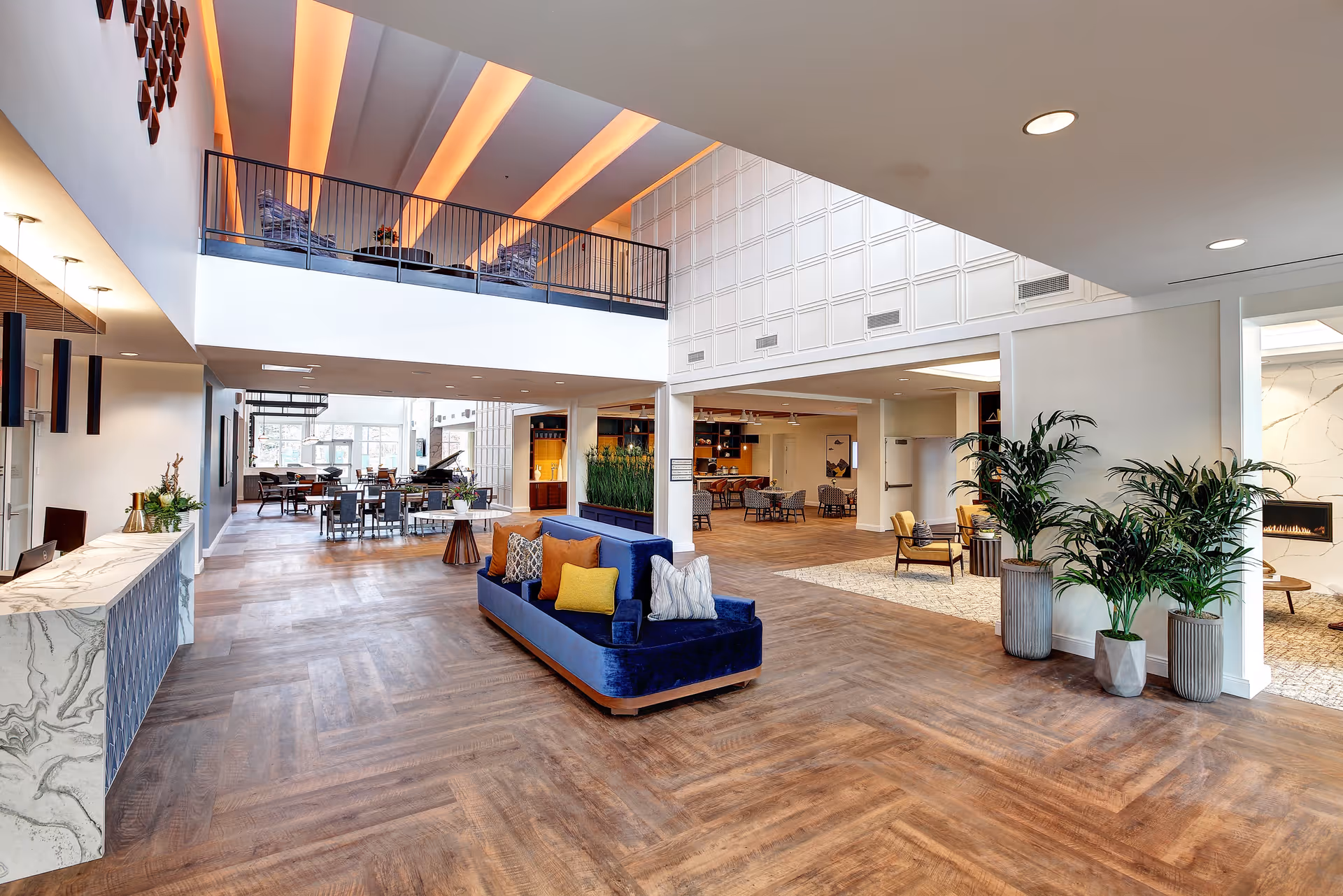 Spacious modern lobby with a blue sofa, multiple seating areas, a mezzanine balcony, and potted plants.