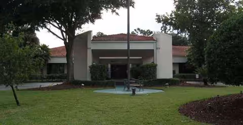 Exterior view of a senior living facility entrance with a fountain and manicured lawn.