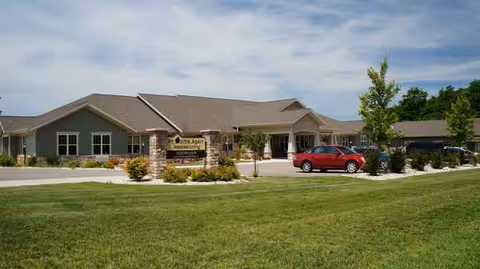 Senior living facility exterior with a sign, landscaped yard, and a red car in front.