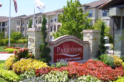 Entrance sign reading "Parkview in Frisco" surrounded by colorful flowerbeds with the senior living buildings in the background.