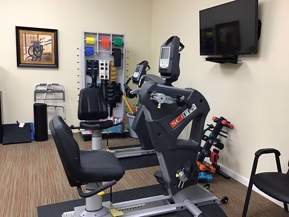 Small fitness room with two recumbent exercise bikes, free weights, resistance bands and a wall-mounted TV.