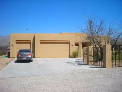 Tan stucco senior living facility with three garage doors, gated entrance, and a car in driveway.