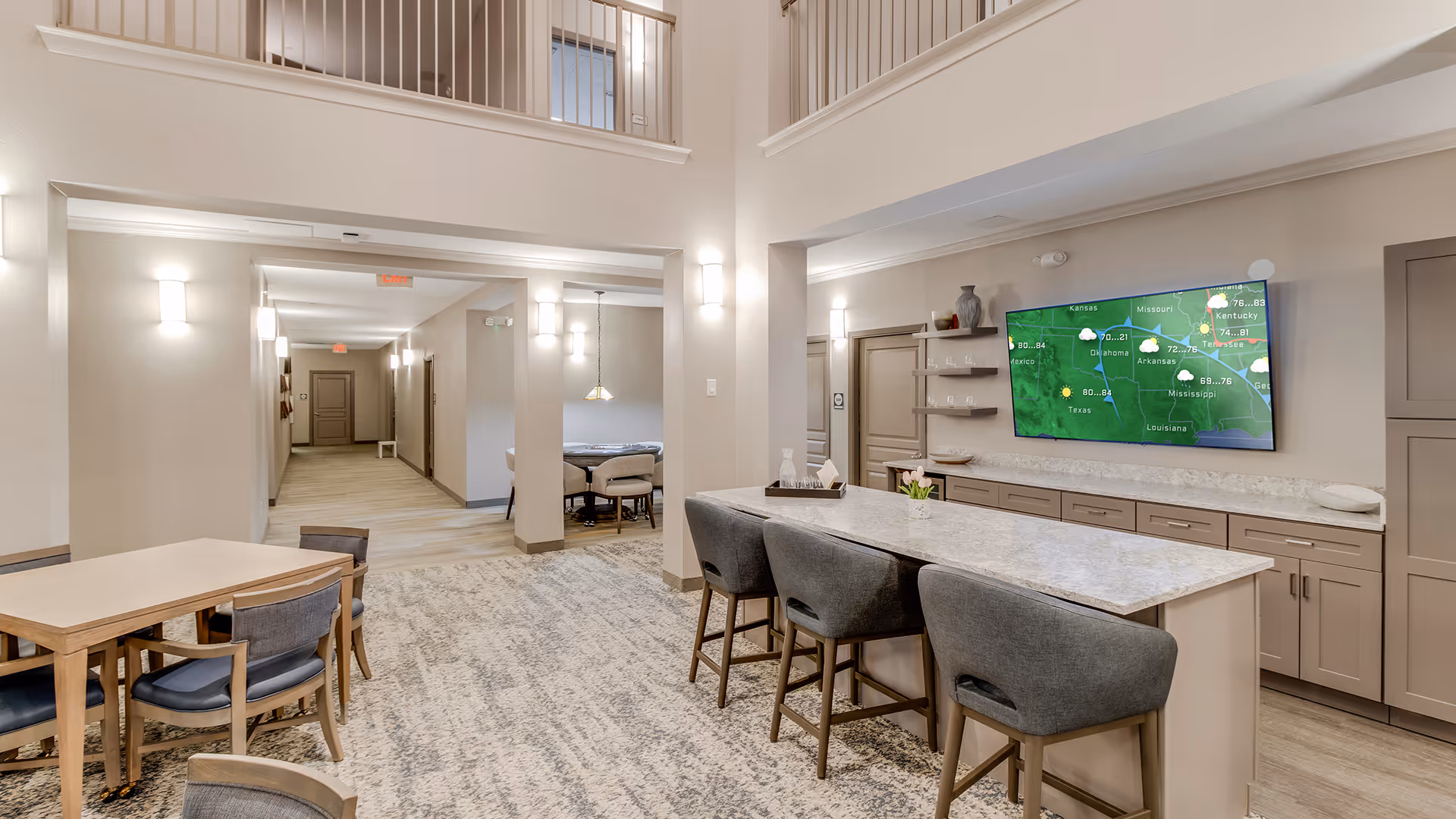 Bright, modern senior living common area with an island countertop and bar stools, a wall-mounted TV, and dining tables.