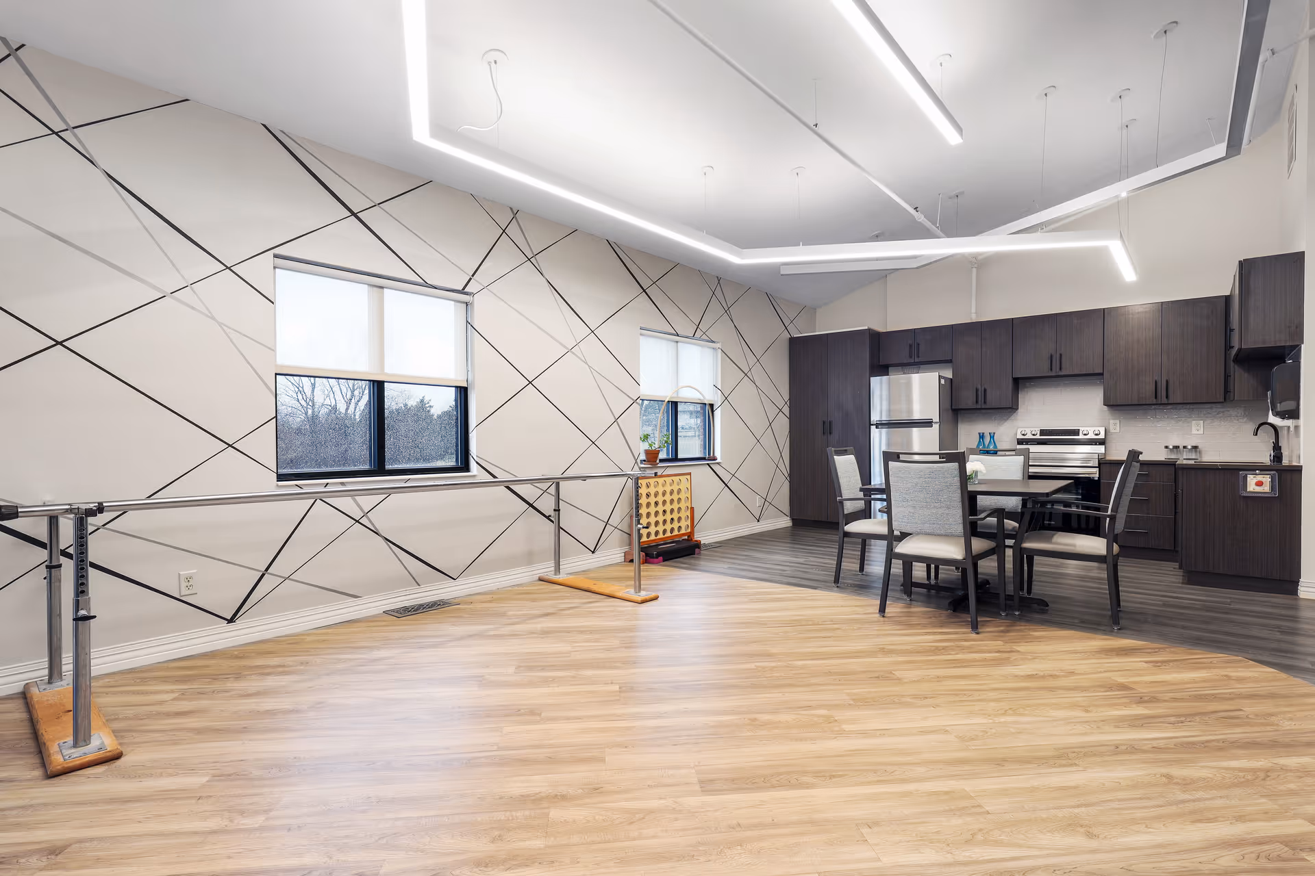 Bright multipurpose interior showing a kitchen and dining table beside parallel therapy bars and a patterned accent wall.