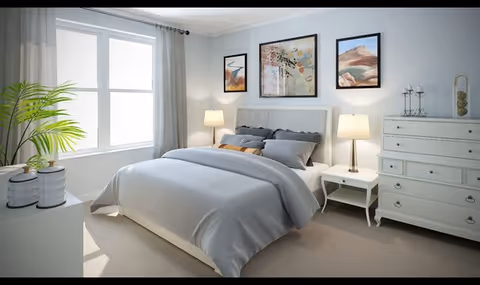 A bright and neatly arranged bedroom with a large bed covered in light gray bedding, two bedside tables each with a lamp, a white dresser, three framed artworks on the wall above the bed, a window with sheer curtains, and a green plant on a white cabinet.