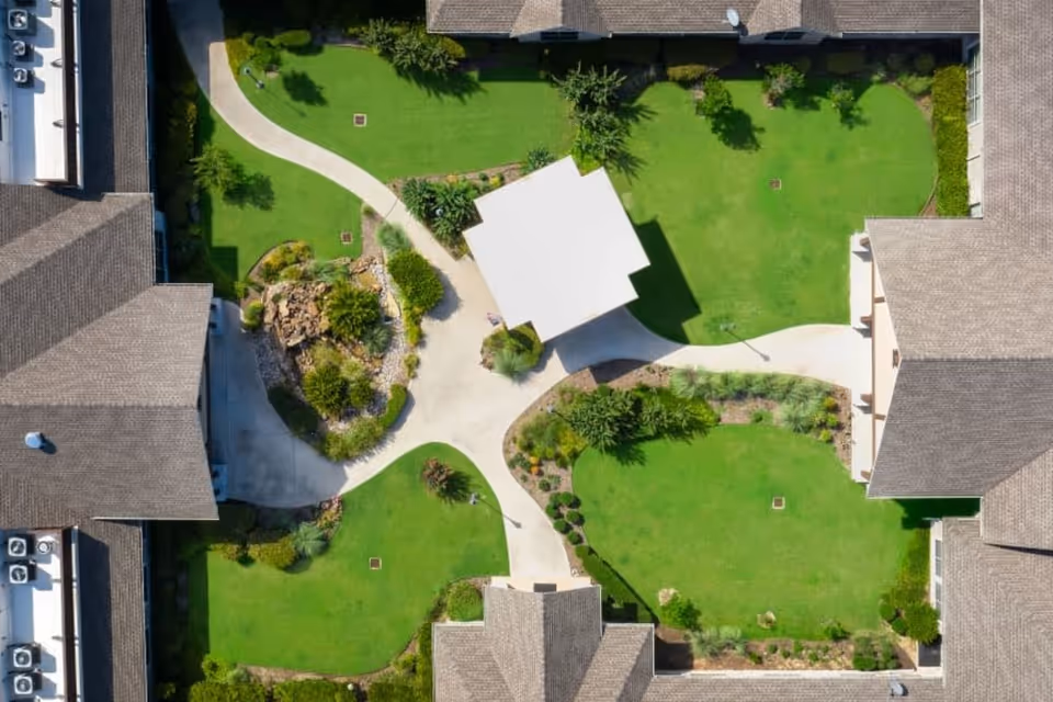 Aerial view of a landscaped central courtyard with green lawns, winding pathways, a small pavilion, and surrounding buildings.