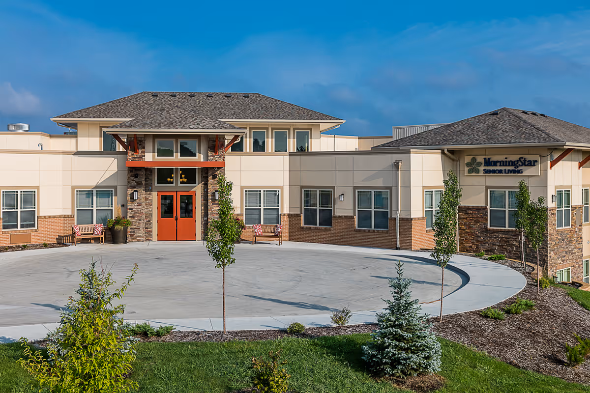 Exterior view of MorningStar Assisted Living & Memory Care at Jordan Creek building with a circular driveway, landscaped greenery, and clear blue sky.