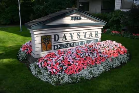 A flower-bordered sign reading DayStar Retirement Village sits on a green lawn.