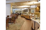Well-lit dining room with buffet serving stations on the right and tables and chairs on the left.