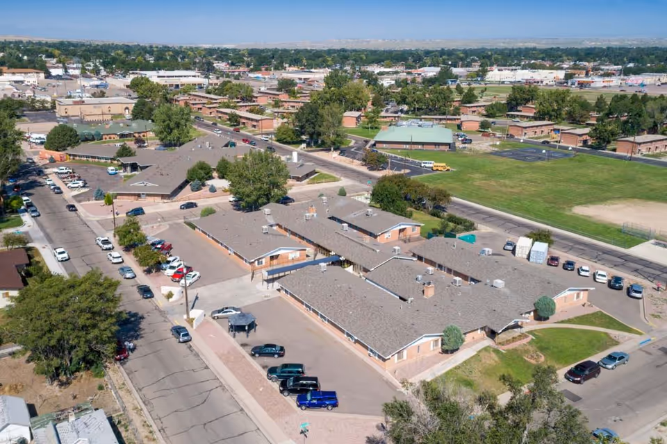 Aerial view of a single-story post-acute and rehabilitation facility complex with multiple parking areas, surrounding streets, and nearby green fields.