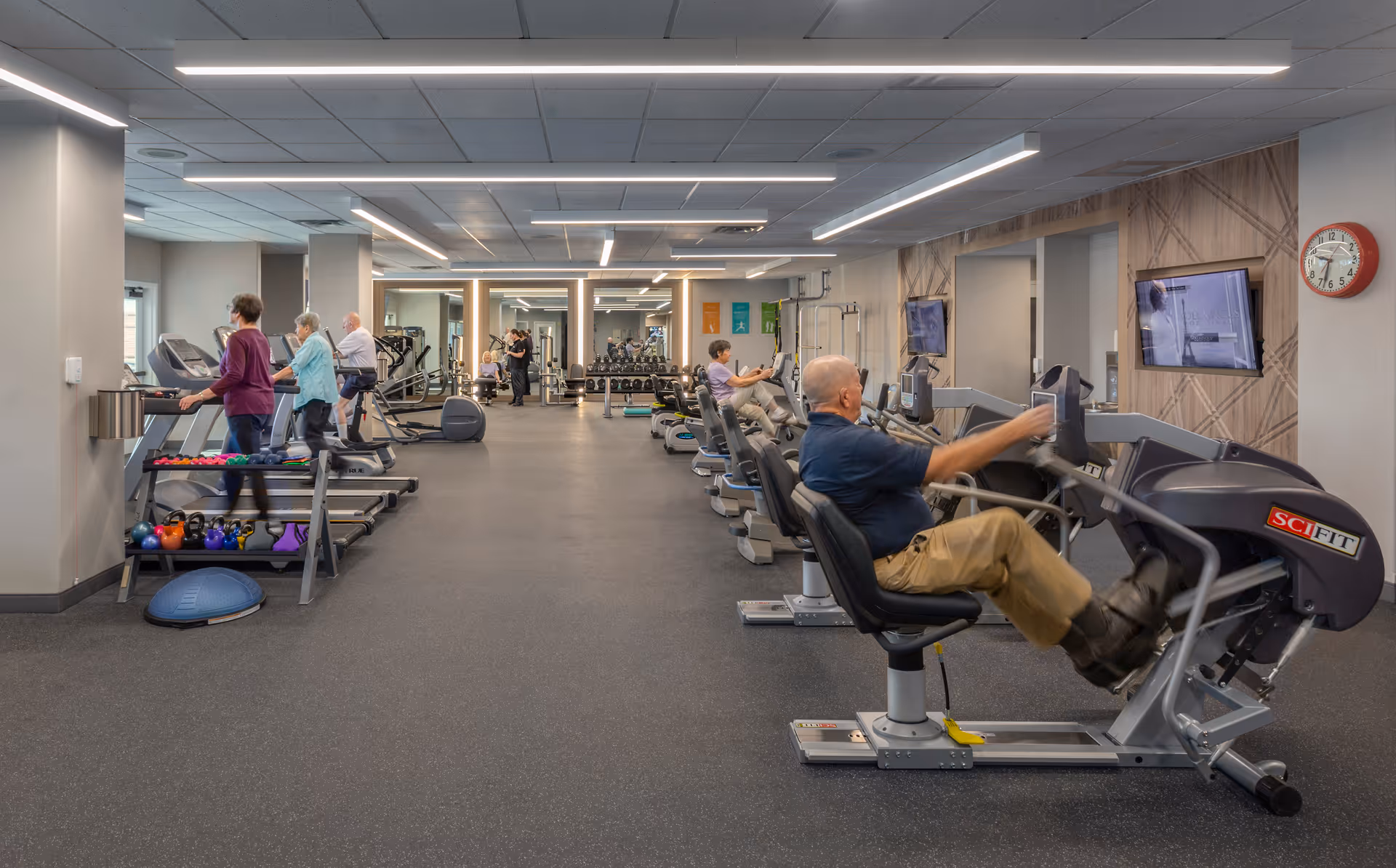 Residents exercising on recumbent bikes and treadmills in a senior living facility fitness center.