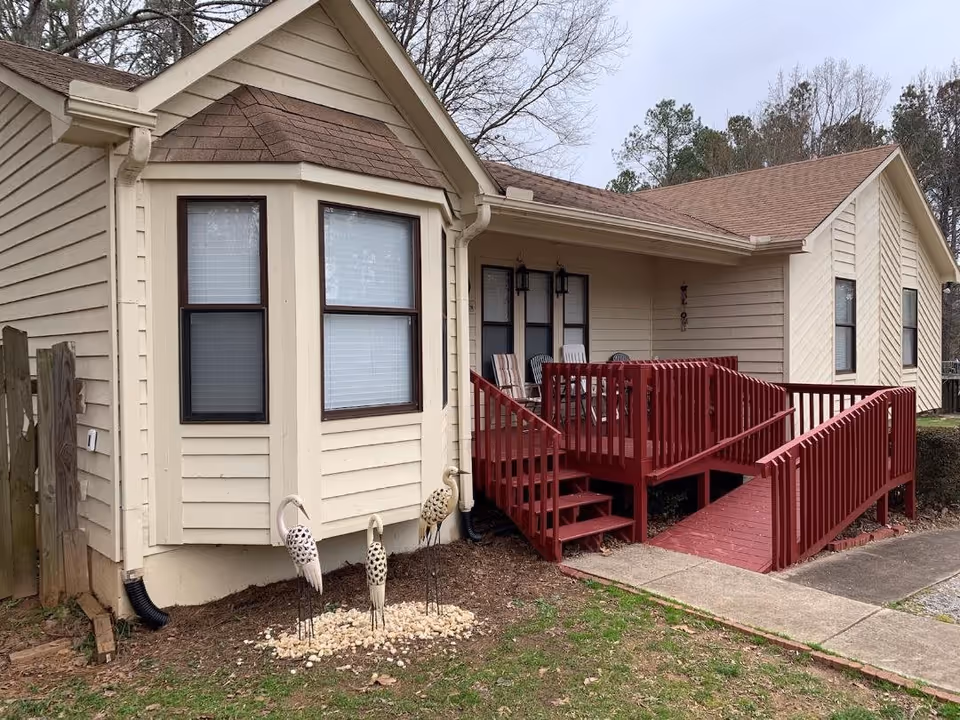 Front exterior of a beige single-story house with a red wooden ramp and small porch.