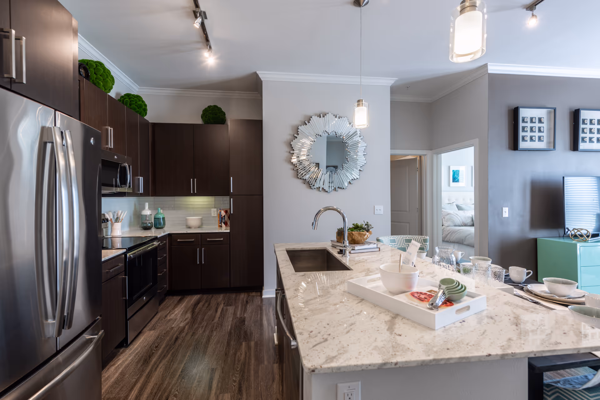 Open-concept modern kitchen with a marble island, stainless steel appliances, dark cabinets, and a decorative wall mirror.