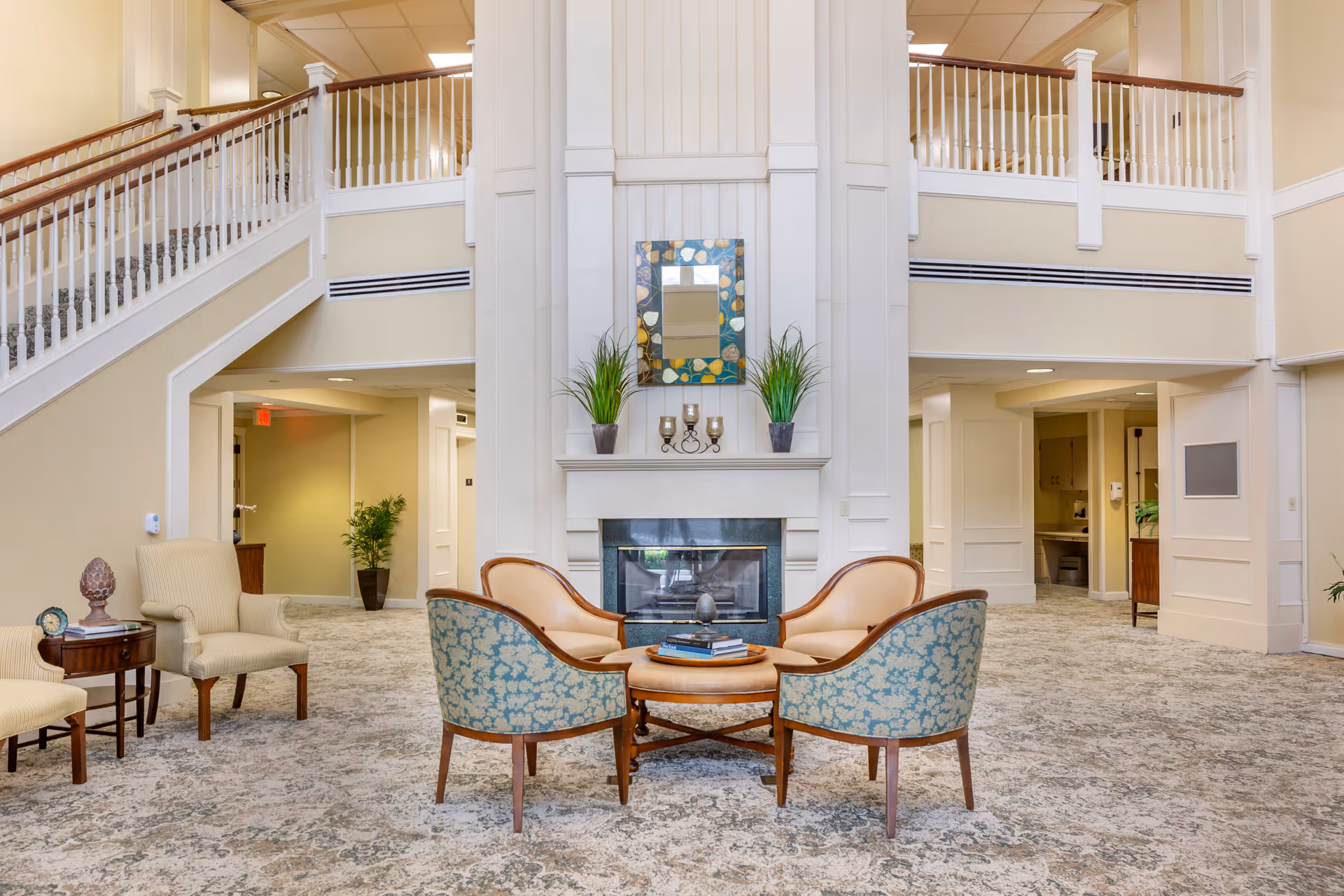 Two-story communal lounge with a fireplace, a cluster of chairs and a staircase overlooking the seating area.