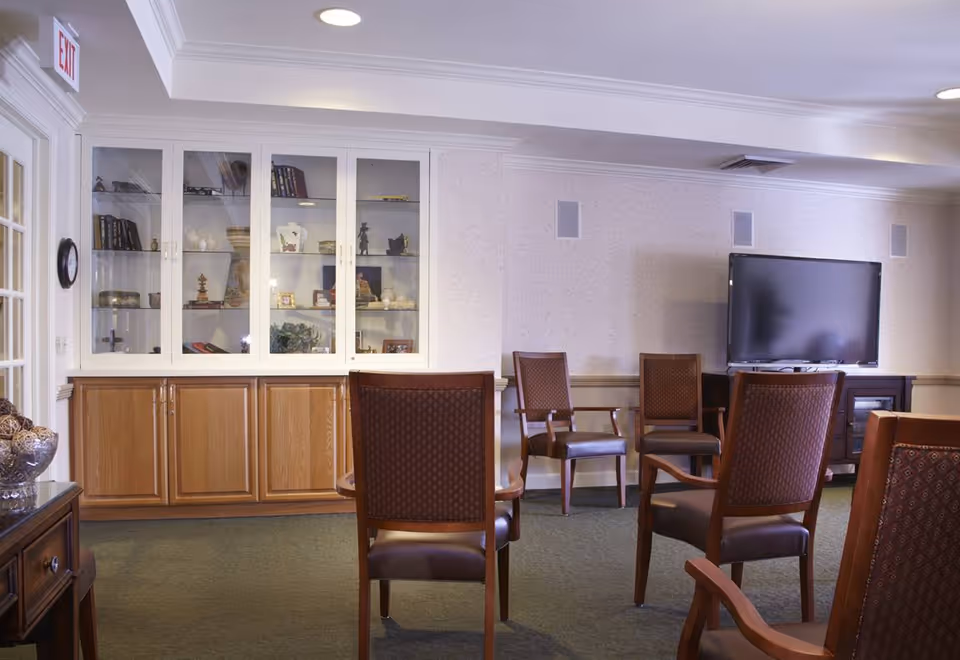 Seating area in a senior living community with arranged chairs facing a television and built-in display cabinets.