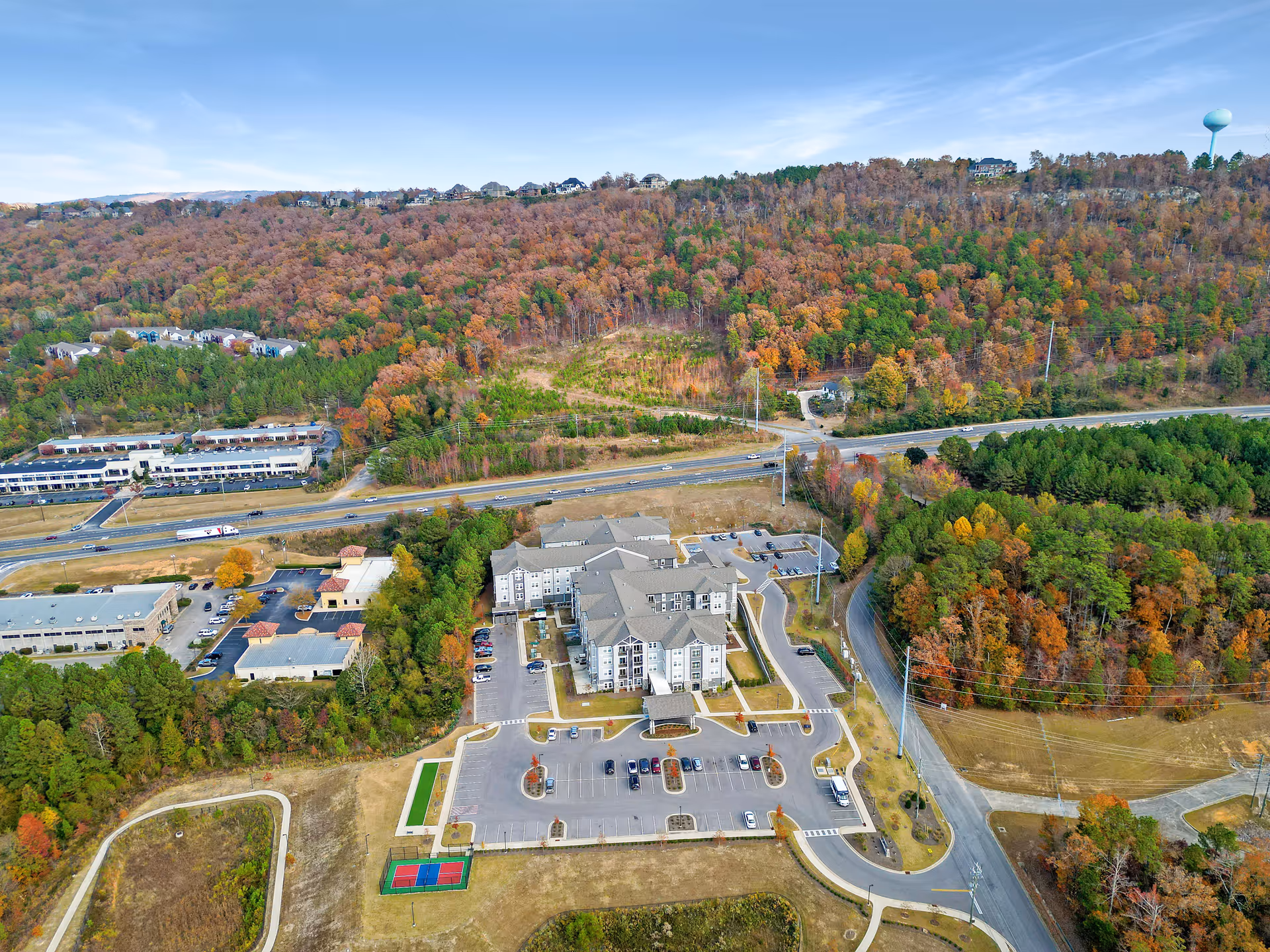 Aerial view of Monark Grove Greystone facility surrounded by trees with autumn foliage, parking lots, nearby roads, and a water tower in the distance.