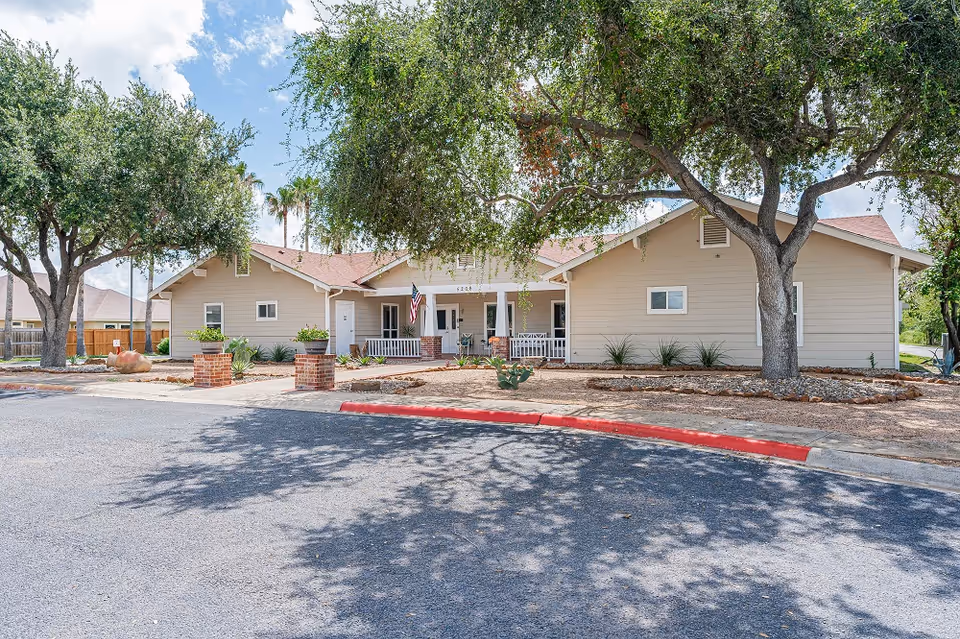 Single-story assisted living facility exterior with entrance porch, trees, and a red curb lined street.