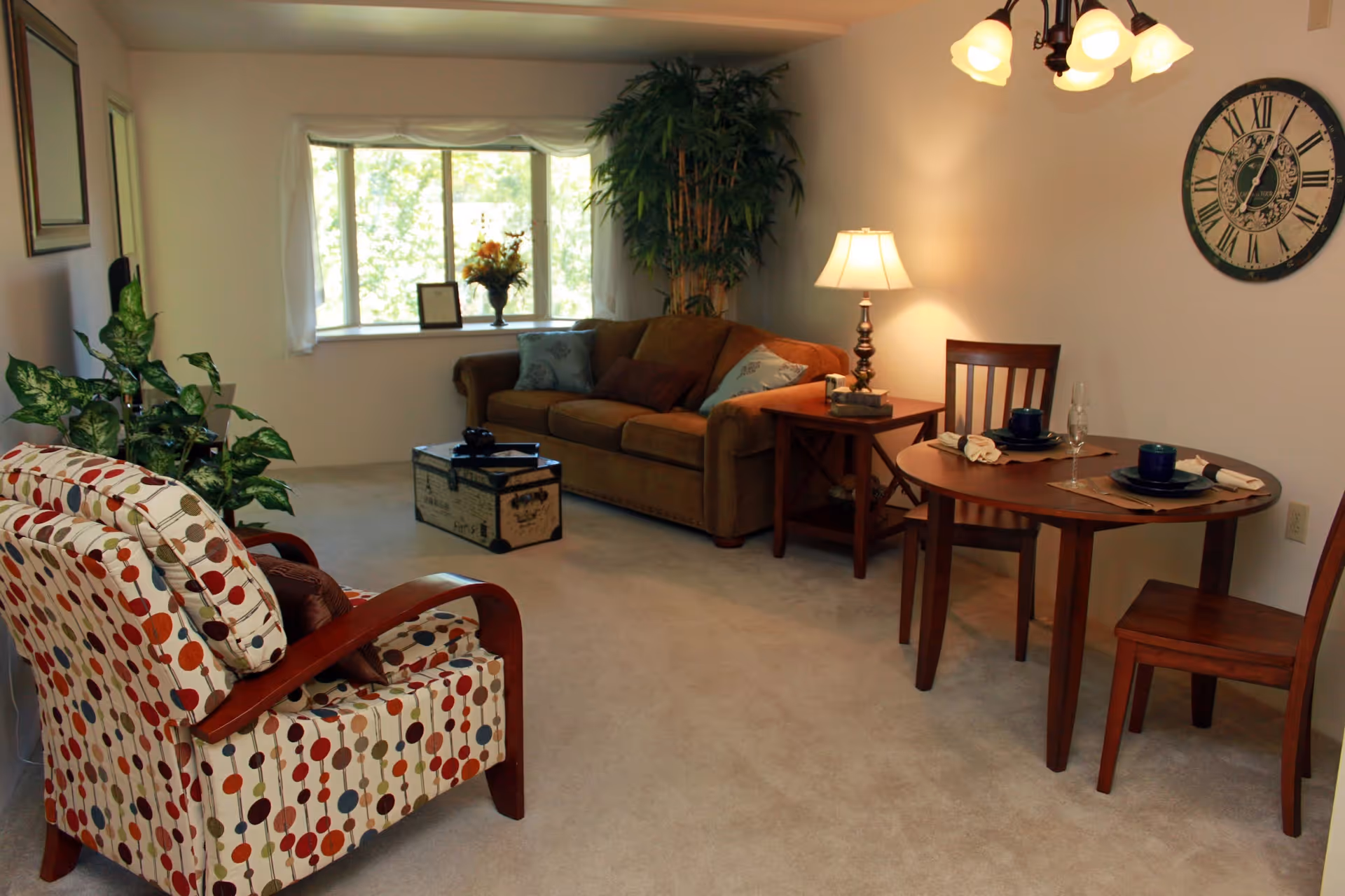 Cozy living room with a patterned armchair, sofa, small round dining table, and a large wall clock.