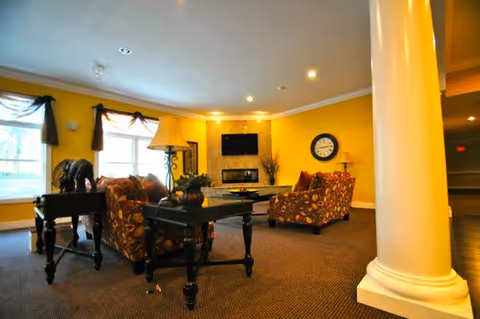 Bright yellow living room with patterned armchairs, a dark coffee table, lamps, and a fireplace.