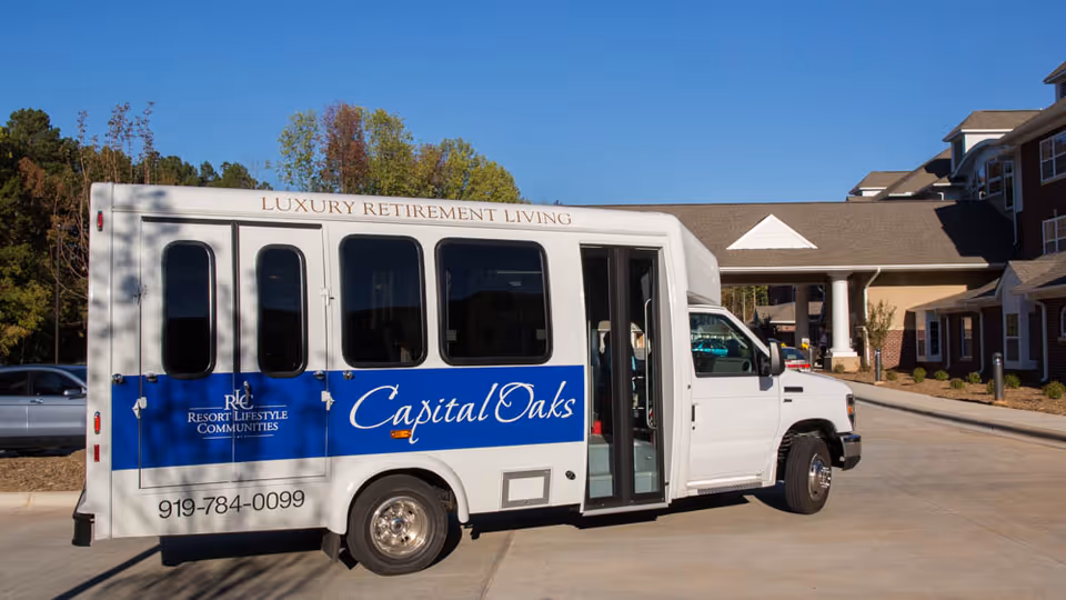 White Capital Oaks retirement shuttle parked in front of the facility's covered entrance.