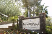 Stone entrance sign reading "Palm Terrace Care Center" set among landscaped flowers, palm trees, and greenery.