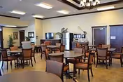 A communal dining area with multiple wooden tables and chairs in a senior living facility.