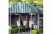 Entrance to a building with a green and white striped awning, surrounded by greenery and bushes.