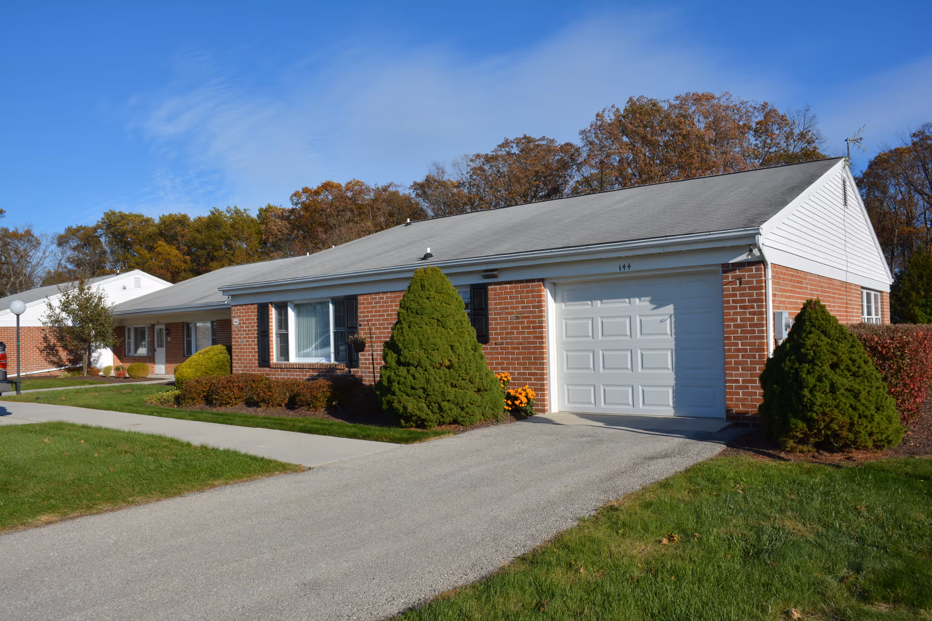 Single-story brick building with a white garage door and a large window, surrounded by green shrubs and a well-maintained lawn under a clear blue sky.
