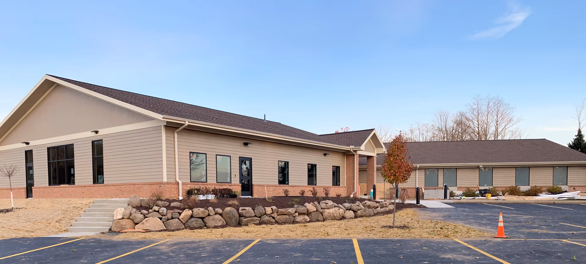 Front exterior of a single-story senior care facility with a parking lot, rock landscaping, and a traffic cone.