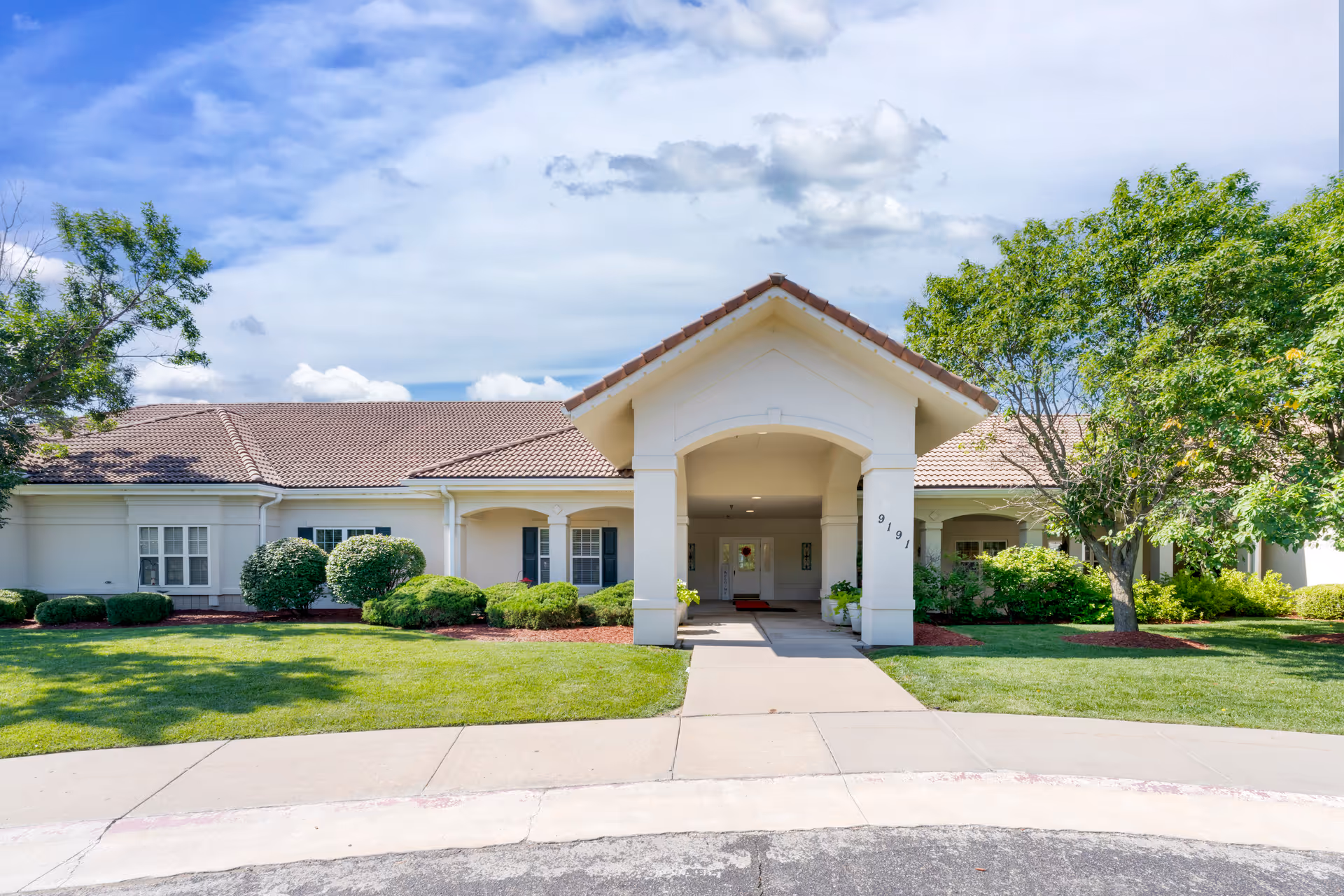A view of the entrance to Brookdale East Wichita, featuring a charming outdoor area with landscaping and a covered entryway.