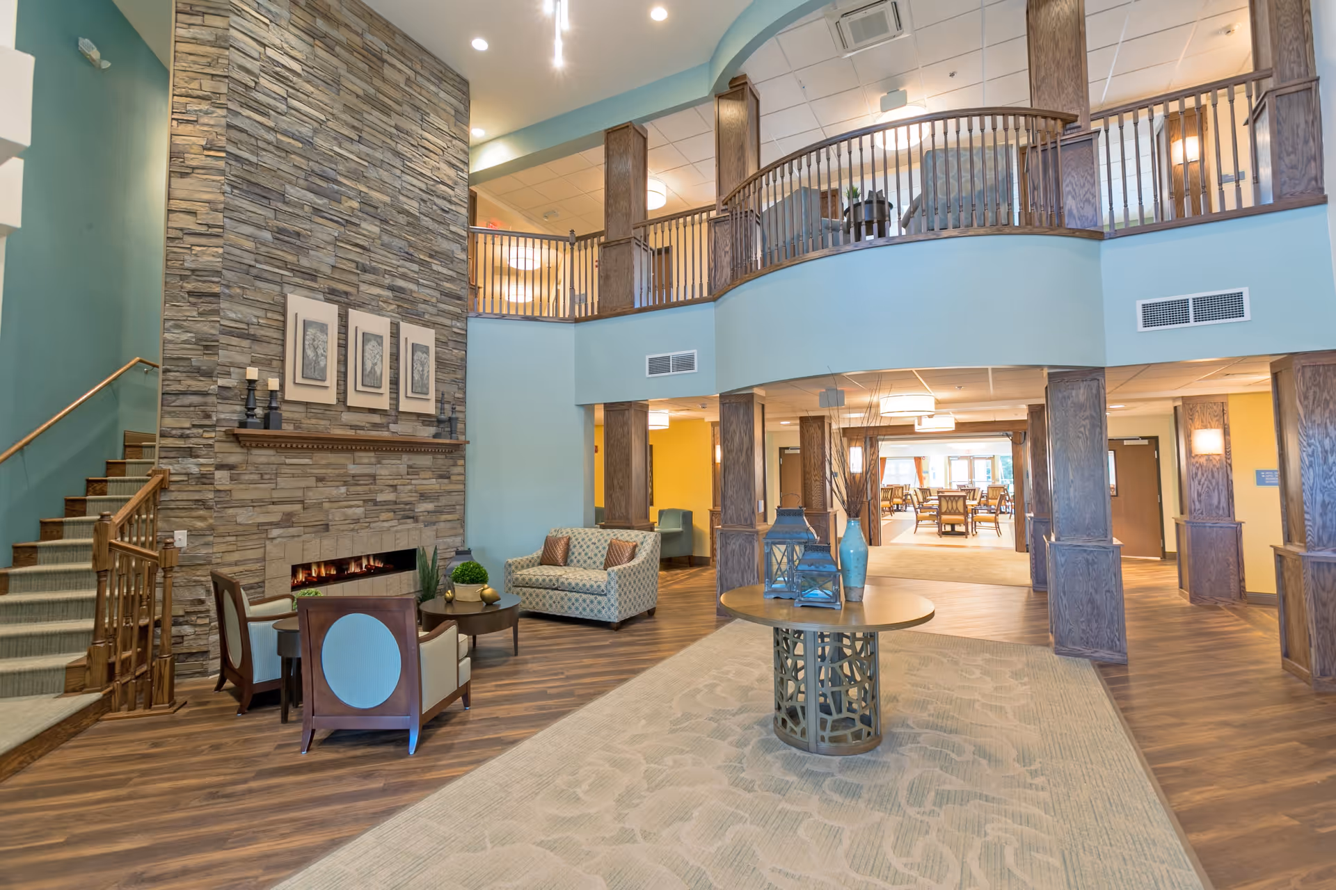 Spacious two-story lobby with seating, a stone fireplace, central round table display, and an upper balcony overlooking the area.