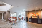 Bright indoor dining area with round tables, red chairs, brick columns, and a reception counter.