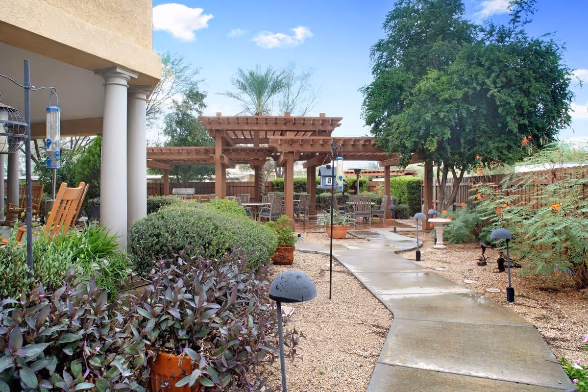 Outdoor courtyard with a paved walkway, garden beds, seating under wooden pergolas and building columns.