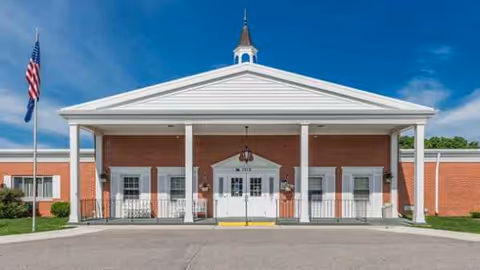 Front entrance of a brick senior living facility with white columns and a portico.