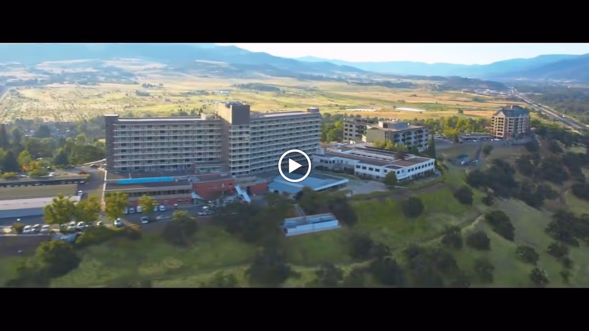 Aerial view of a large multi-story senior living complex on a hillside with surrounding buildings and valley scenery.