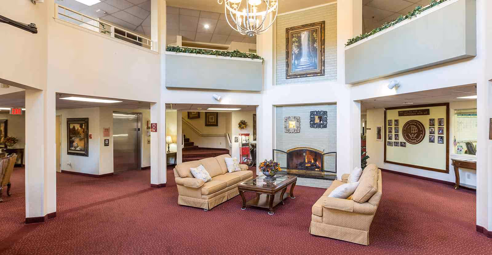 Two-story common area with upholstered sofas around a coffee table facing a fireplace under a chandelier.