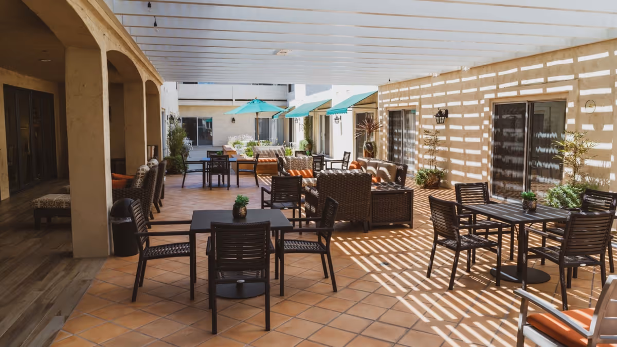 Shaded outdoor courtyard with multiple dining tables, chairs and lounge seating under a pergola.