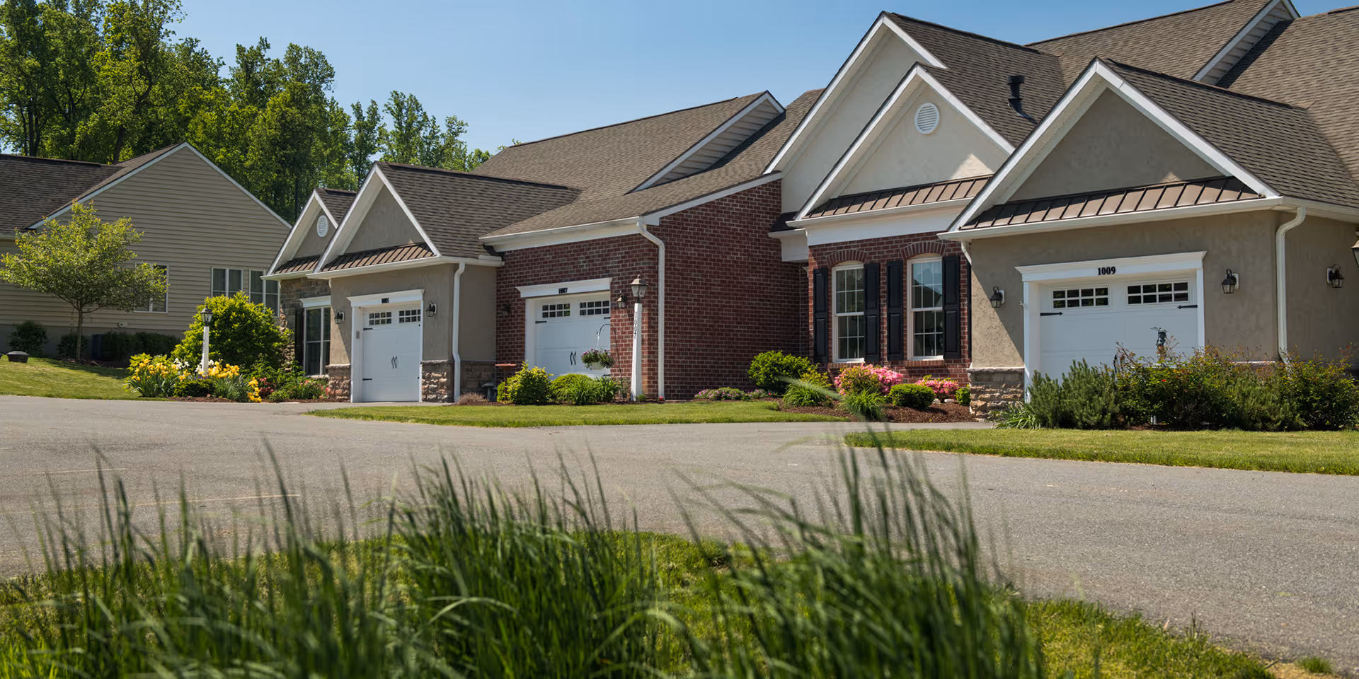 Row of single-story retirement community homes with attached garages, manicured lawns, and landscaping under a clear sky.