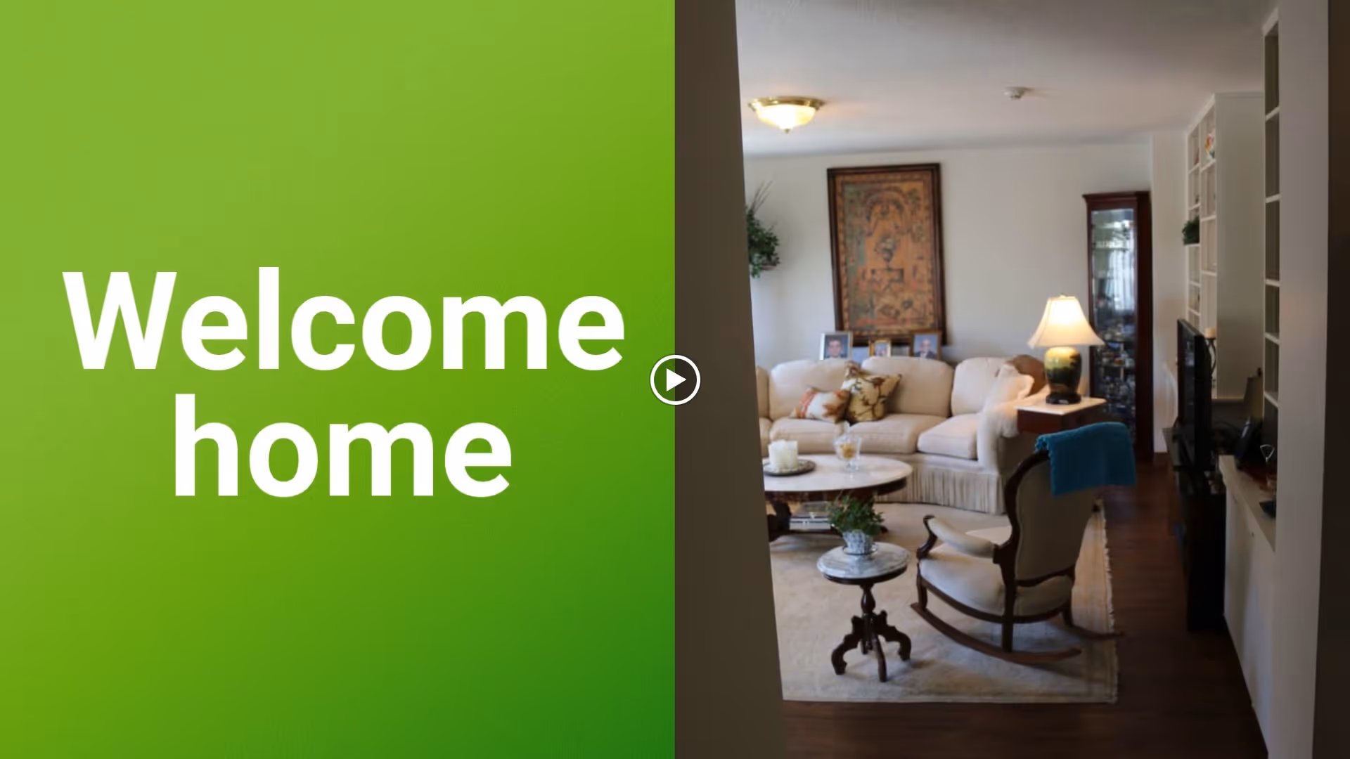 A cozy living room with a beige sectional sofa adorned with pillows, a round coffee table with decorative items, a rocking chair with a blue throw, a side table with a lamp, and a framed artwork on the wall. The room has wooden flooring and built-in shelves with a TV.