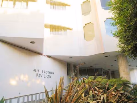 White hospital exterior with entrance, plants in foreground, and Alix Botman Pavilion sign.