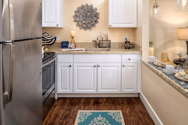 Small modern kitchen with stainless steel refrigerator and stove, white cabinets, granite countertops, a sink, and a decorated breakfast bar.