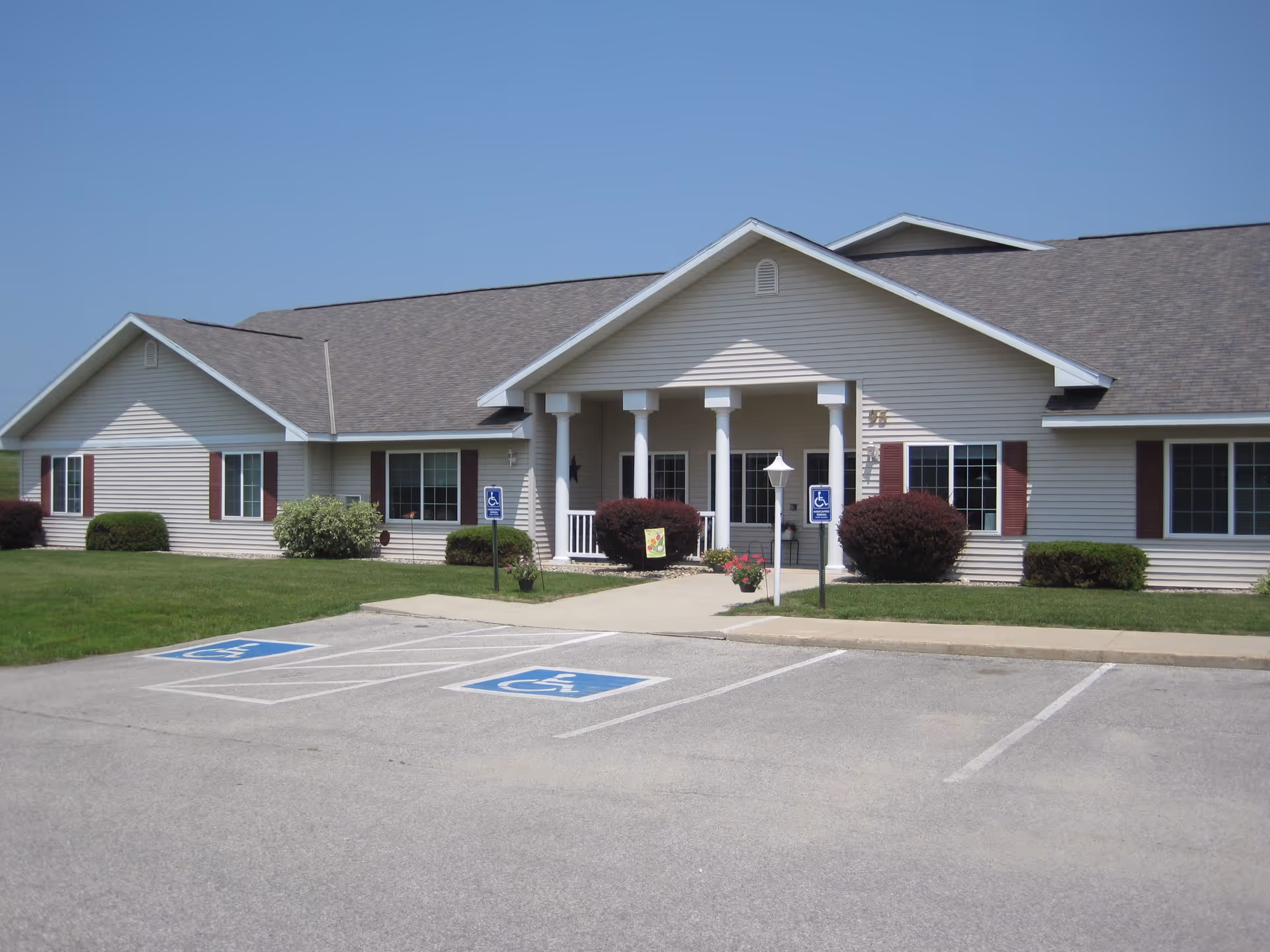Single-story beige building with a columned entrance, landscaped lawn, and two accessible parking spaces in front.
