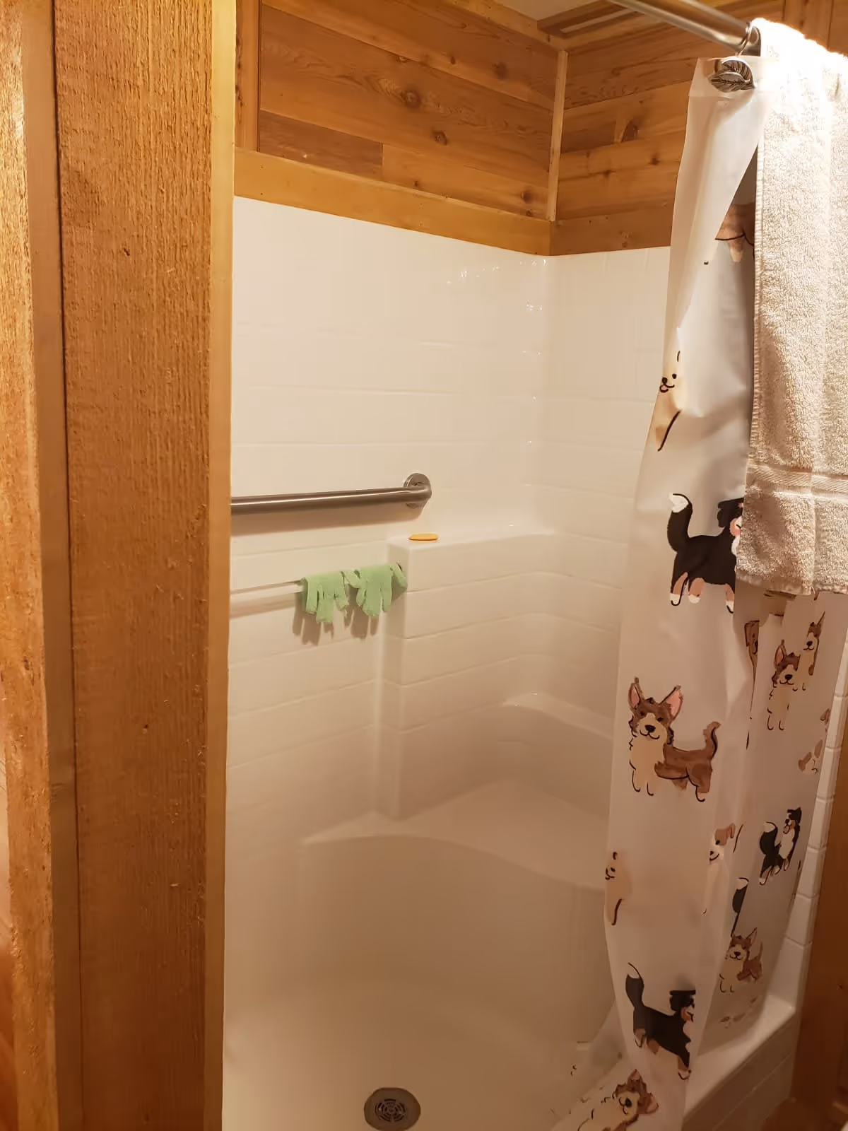 Shower stall with white tile surround, built-in seat and grab bar, wood trim and a dog-print shower curtain.