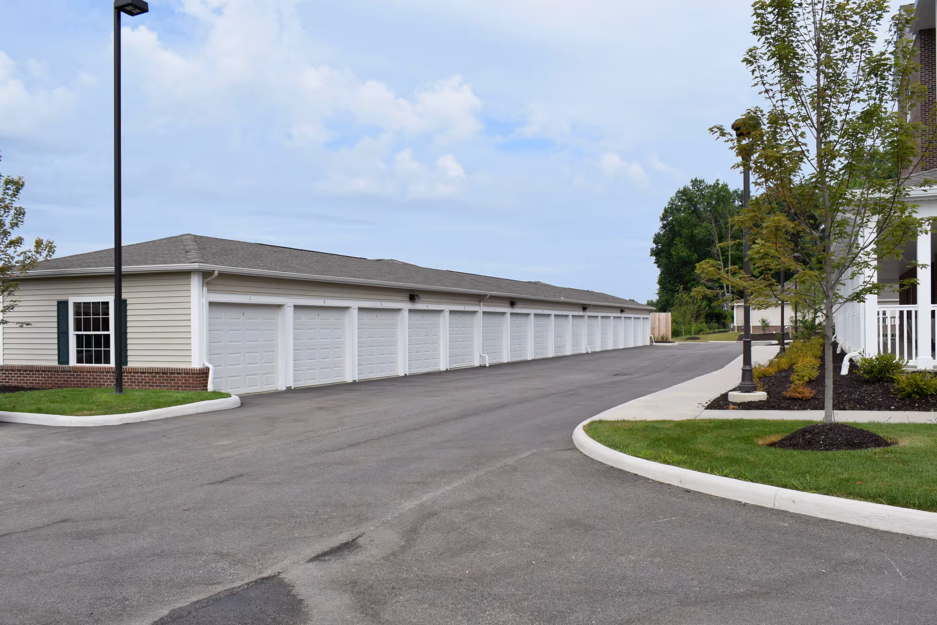 Row of white garage doors along a single-story building with a paved driveway, landscaped curbs, and lamp posts.