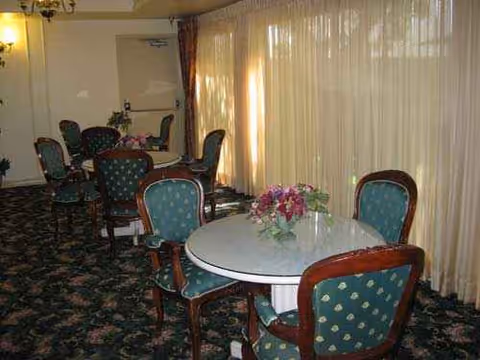 Senior living facility dining room with round tables, green upholstered chairs, and sheer curtains.